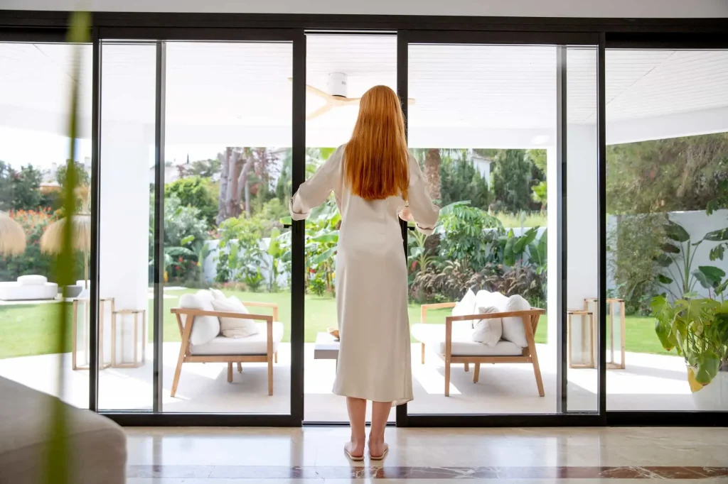 Person opening sliding glass door to a lush garden area