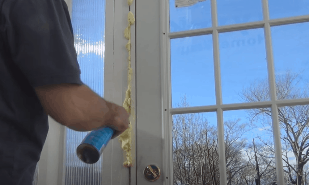 Man applying foam insulation to a glass door