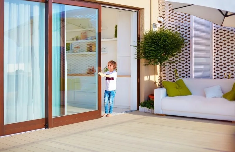 Child opening large sliding glass door to patio