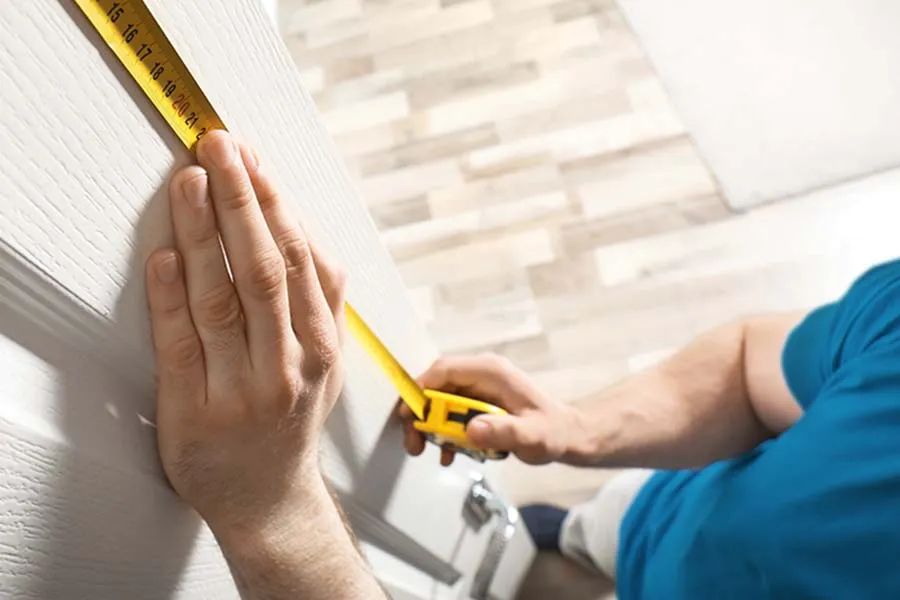 Personne mesurant la hauteur d'une porte avec un ruban à mesurer jaune