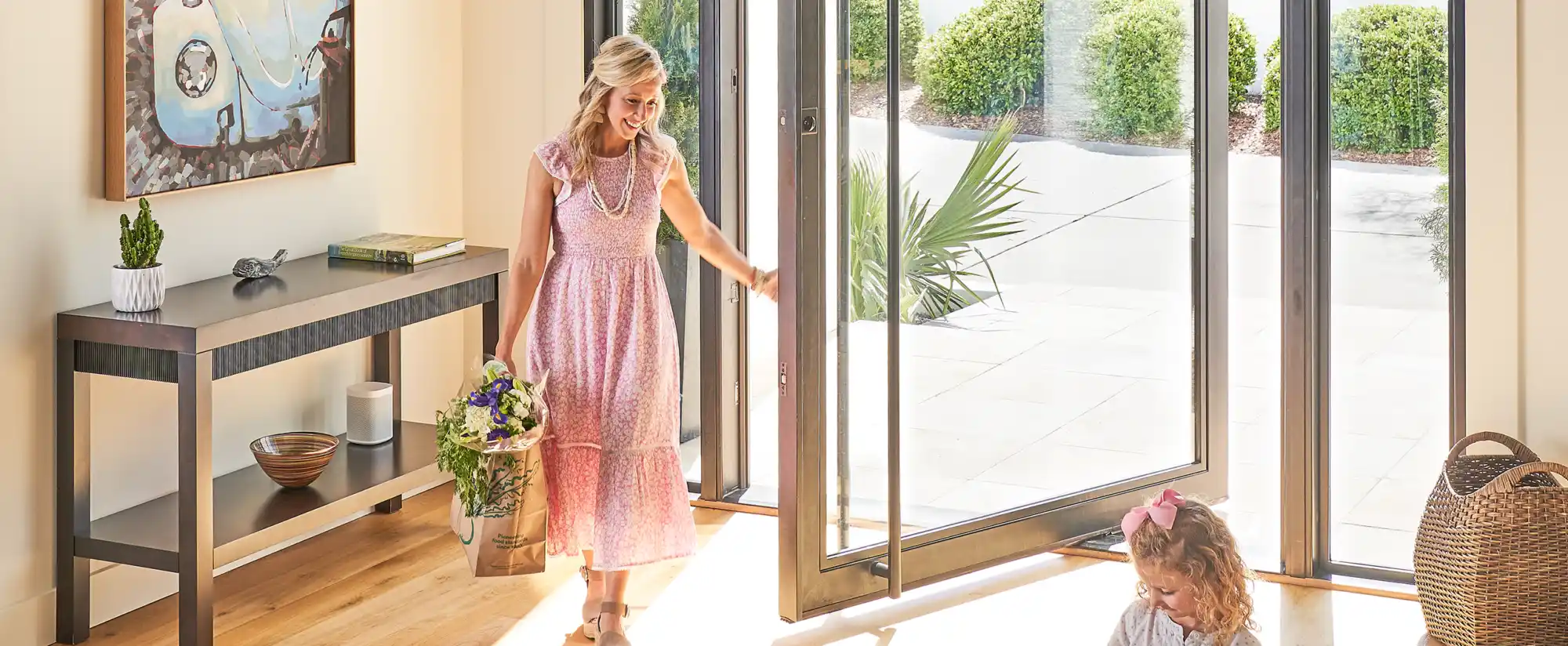 Woman opens pivot door while child plays on sunlit floor