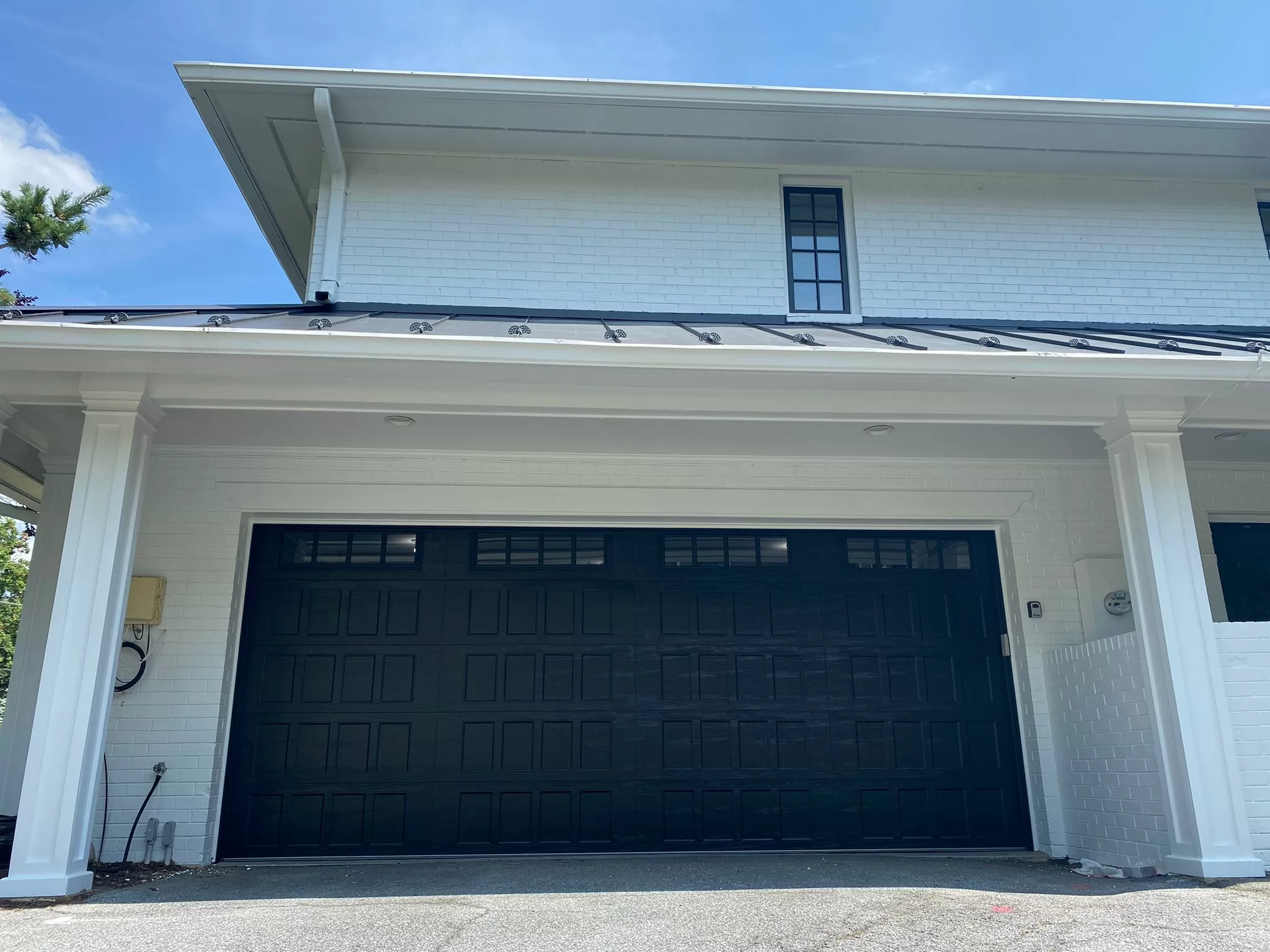 Puerta de garaje con paneles negros en el exterior de una casa de ladrillo blanco