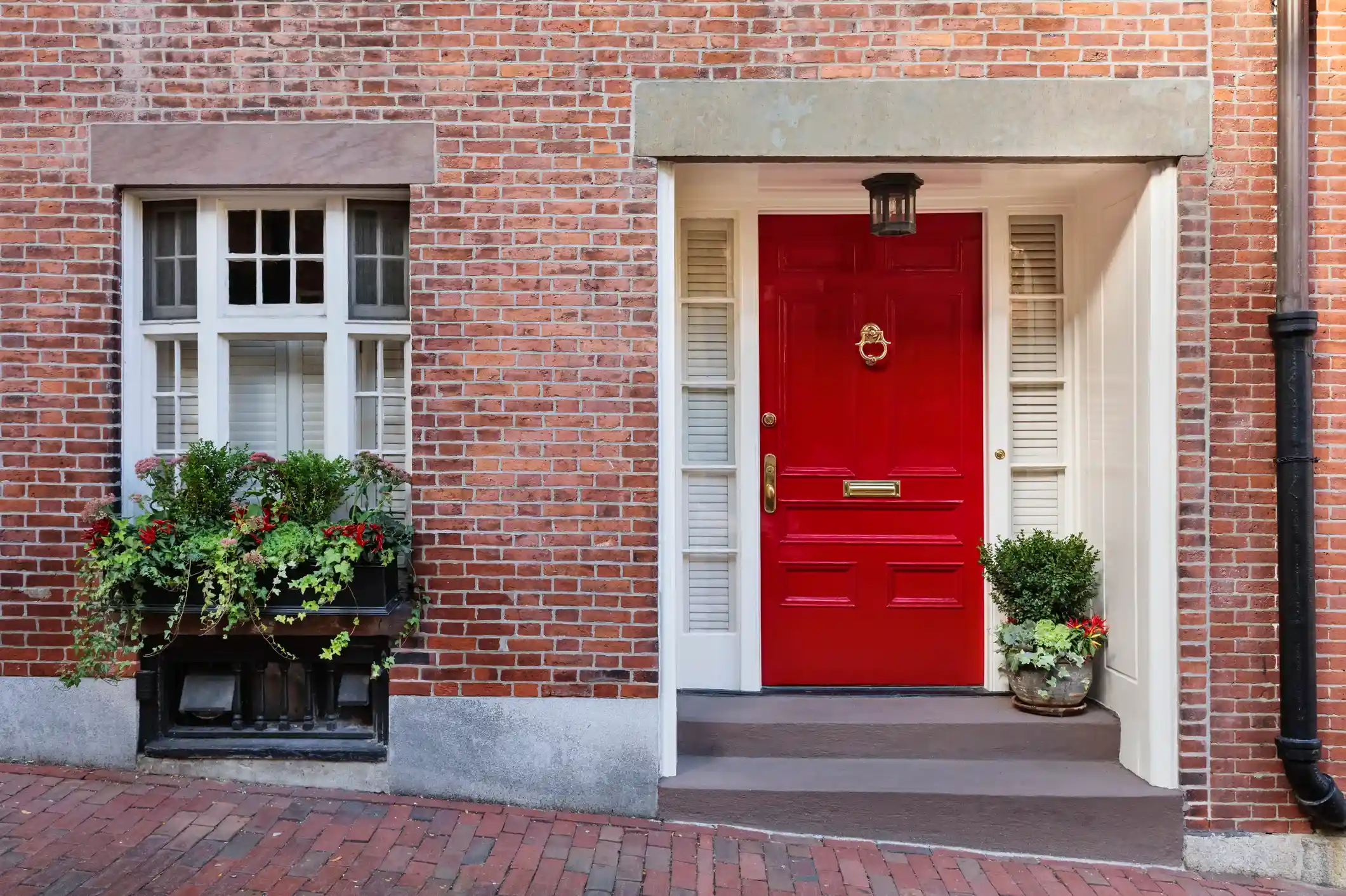 Bold red front door on brick home with potted plants