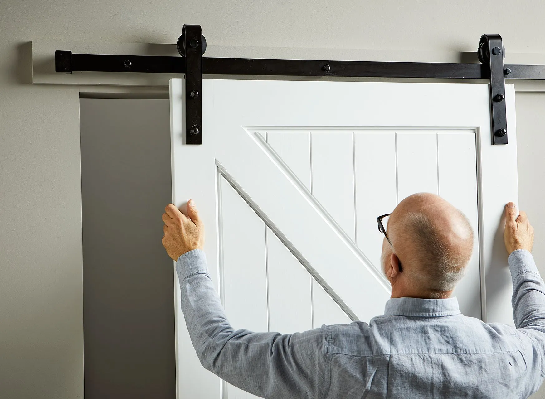 Мужчина устанавливает белую дверь амбара на черную подвесную направляющую