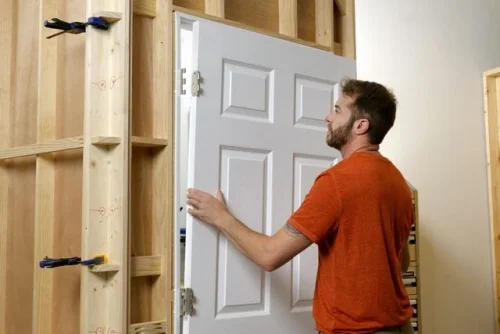 Man lifting white door from newly built frame