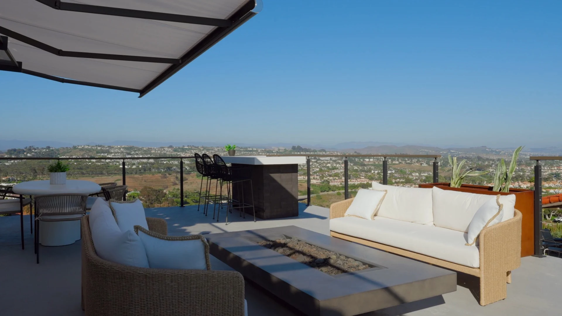 Luxury upper-level outdoor sun deck with glass railing, fire pit, and seamless ocean breeze vistas in California